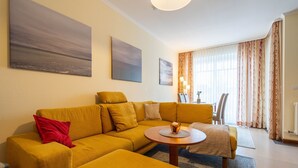 A modern living room with a yellow sofa, a coffee table, and a dining area with chairs and a table. - Komfort Ferienwohnung mit 2 Schlafzimmern und Balkon im Dachgeschoss (Ostseebad Binz)