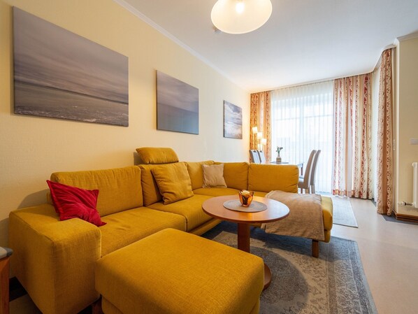 A modern living room with a yellow sofa, a coffee table, and a dining area with chairs and a table.