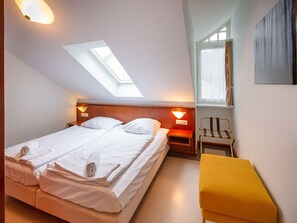A hotel room with a bed, a bench, a nightstand, and a skylight.