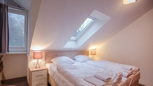 Ein Schlafzimmer mit Dachfenster, einem Bett, zwei Nachttischen mit Lampen und einem Holzboden.
