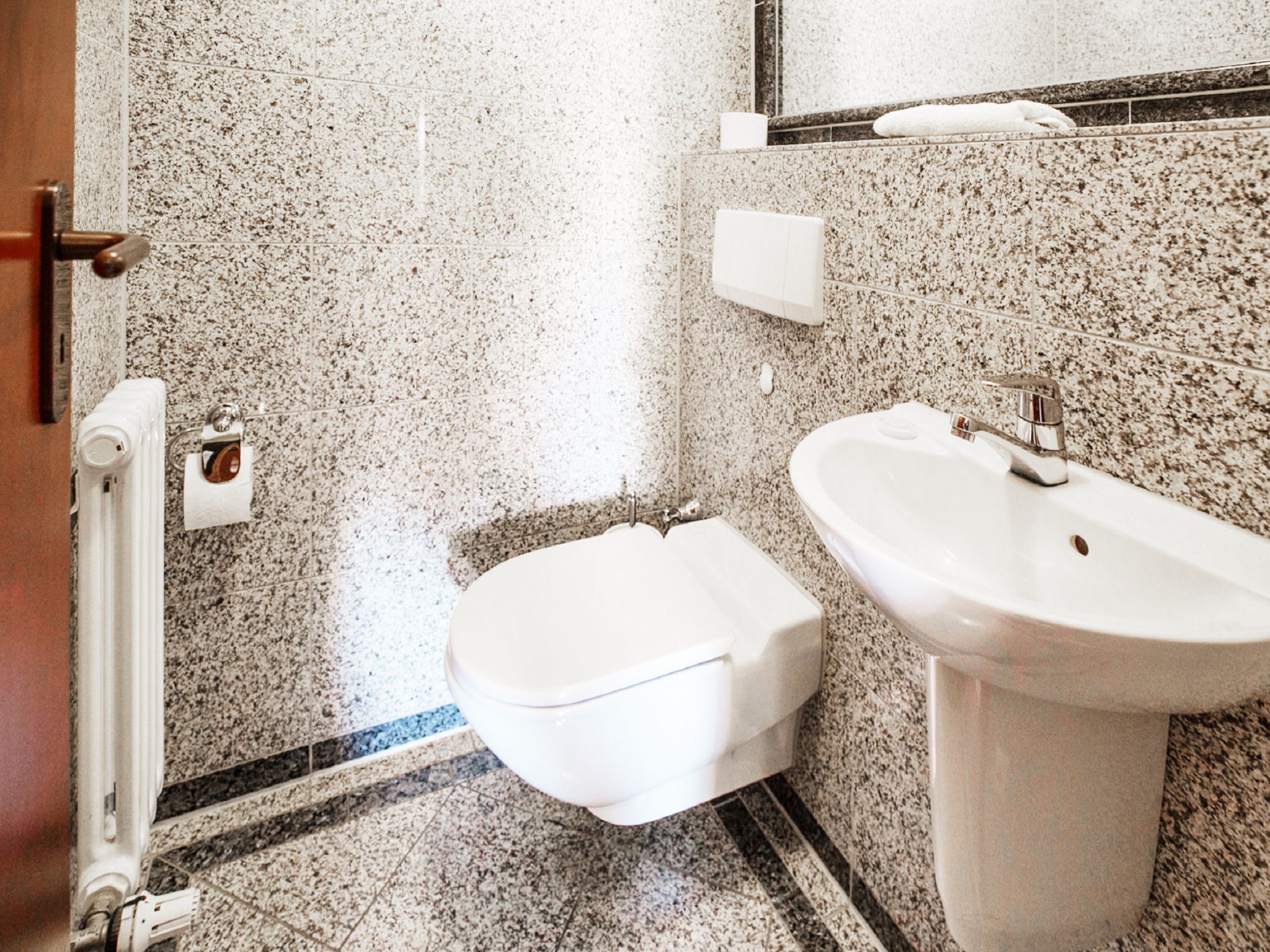 A bathroom with a toilet, sink, and marble walls.