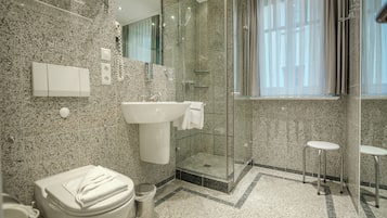 A modern bathroom with a granite countertop, a sink, a toilet, a glass shower enclosure, and a small stool.