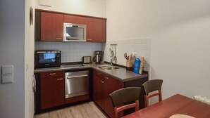 Cozinha compacta com eletrodomésticos de aço inoxidável, pia e área de jantar com duas cadeiras.