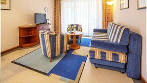 A living room with a sofa, armchairs, a coffee table, a TV, and a clock on the wall. - Comfort apartment with 1 bedroom and balcony on the upper floor (Ostseebad Binz)