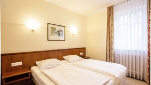 A hotel room with two beds, a wooden headboard, a nightstand, a framed picture on the wall, and a window with sheer curtains. - Comfort apartment with 1 bedroom and balcony on the upper floor (Ostseebad Binz)