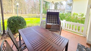 Un porche cubierto con una mesa y sillas de madera, una parrilla y vistas a un jardín y árboles.