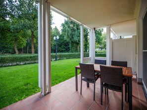 A covered patio with a table and chairs, overlooking a well-maintained garden and trees. - Komfortplus Ferienwohnung mit 1 Schlafzimmer und Terrasse im Erdgeschoss (Ostseebad Binz)