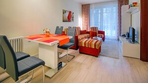 Una sala de estar moderna con comedor, que incluye una mesa blanca, sillas negras, un conjunto de sofá rojo y un televisor sobre un mueble.