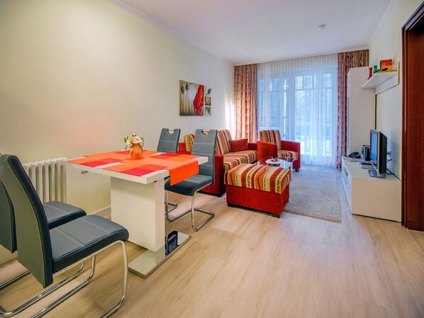 A modern living room with a dining area, featuring a white table, black chairs, a red sofa set, and a television on a stand. - Komfortplus Ferienwohnung mit 1 Schlafzimmer und Terrasse im Erdgeschoss (Ostseebad Binz)