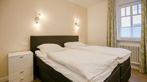 Una cama doble con ropa blanca, una mesita de noche con cajones y dos lámparas de pared.