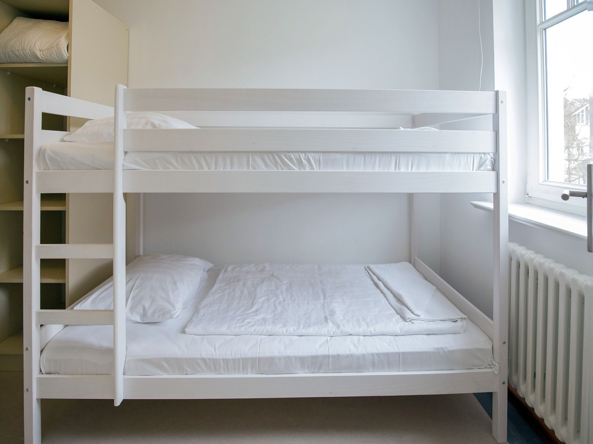 A bunk bed with white bedding in a room with a window and a radiator.