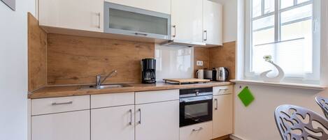 A compact kitchen with white cabinets, a wooden countertop, a built-in microwave, a coffee maker, and a kettle.