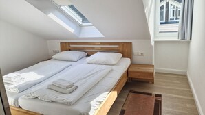 Ein Schlafzimmer mit Oberlicht, einem Bett mit weißer Bettwäsche, einem Holz-Kopfteil, einem Nachttisch und einem Fenster mit Vorhängen.