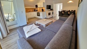 Ein modernes Wohnzimmer mit grauem Sofa, Couchtisch und Fernseher im Hintergrund.