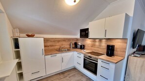 Eine kleine Küche mit weißen Schränken, einer Holz Arbeitsplatte, einem eingebauten Ofen und einer Mikrowelle.