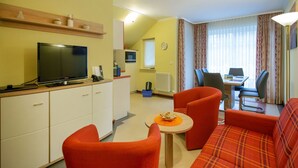 A compact living space with a sofa, two armchairs, a small round table, a television, and a dining area with a table and chairs. - Komfortplus Ferienwohnung mit 2 Schlafzimmern und Balkon im Dachgeschoss (Ostseebad Binz)