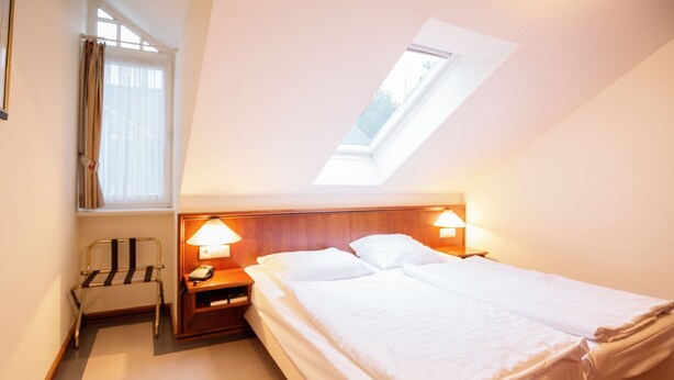 A hotel room with a bed, bedside lamps, a chair, a nightstand, and a skylight. - Komfortplus Ferienwohnung mit 2 Schlafzimmern und Balkon im Dachgeschoss (Ostseebad Binz)