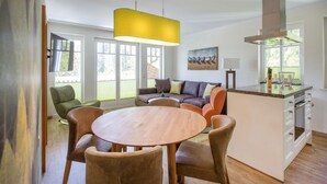 Una cocina moderna con una isla central, un comedor con una mesa redonda y sillas, y un salón con sofá y sillones.