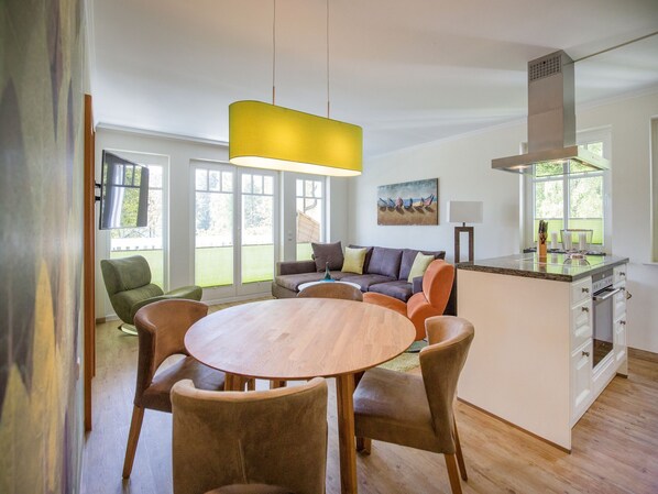 A modern kitchen with a central island, a dining area with a round table and chairs, and a living area with a sofa and chairs.