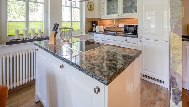 Una cocina moderna con armarios blancos, encimera de granito y estufa empotrada.