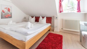 Ein modernes Hotelzimmer mit einem hölzernen Bett, weißer Bettwäsche, einem roten Teppich, einem roten Kopfteil, einem Fenster mit rosa Vorhängen, einem Heizkörper und einem Gemälde von roten Blumen.