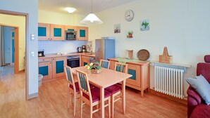 A compact kitchen with wooden cabinets, a dining table with chairs, a refrigerator, and a radiator. - Comfort apartment with 2 bedrooms and terrace on the first floor (Ostseebad Binz)