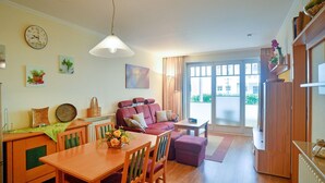 A cozy living room with a wooden dining table, a red sofa, and a large window. - Comfort apartment with 2 bedrooms and terrace on the first floor (Ostseebad Binz)