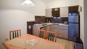 A compact kitchen with a dining table, chairs, a refrigerator, and a hanging light fixture.