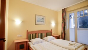 A hotel room with a bed, two bedside tables, a nightstand, a window with curtains, and a wall-mounted picture.