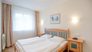 Un letto ben rifatto con lenzuola bianche, una testiera in legno e un comodino con una lampada.