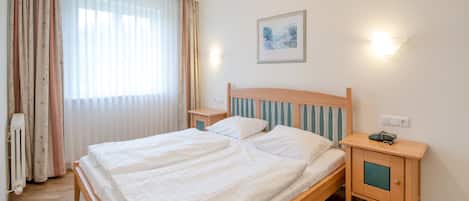 A neatly made bed with white linens, a wooden headboard, and a nightstand with a lamp.