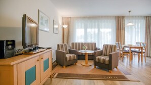 Un soggiorno moderno con una TV a schermo piatto, un mobiletto in legno, divani a righe, un tavolino rotondo e un'area pranzo con tavolo e sedie in legno.