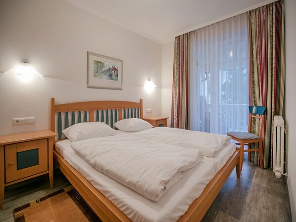 A neatly made bed with white bedding, a wooden headboard, and two bedside tables with lamps. A framed painting hangs on the wall above the bed.
