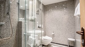 Une salle de bain moderne avec une douche à parois de verre, des toilettes blanches, un lavabo et un petit tabouret.