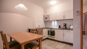 Une cuisine compacte avec des meubles blancs, un four à micro-ondes, un four et une machine à café. On y trouve une table à manger en bois avec des chaises.