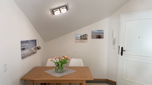 A dining area with a wooden table, white chairs, and a vase of flowers. There are wall-mounted pictures and a white door. - Comfort apartment with 2 bedrooms and balcony on the top floor (Ostseebad Binz)