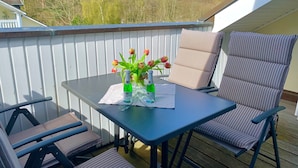 A deck with a table and chairs, a vase with tulips, and a view of trees. - Comfort apartment with 2 bedrooms and balcony on the top floor (Ostseebad Binz)