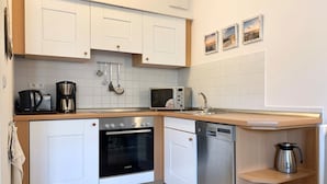 A compact kitchen with white cabinets, a Bosch oven, a microwave, and a coffee maker. - Comfort apartment with 2 bedrooms and balcony on the top floor (Ostseebad Binz)