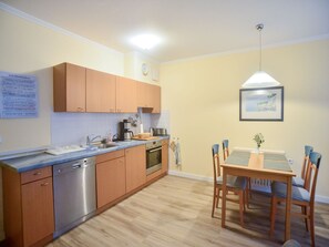 A kitchen with wooden cabinets, a dishwasher, and a dining area with a table and chairs.