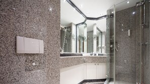 Un baño moderno con paredes de granito, un inodoro blanco, una ducha con cerramiento de vidrio y un espejo grande.