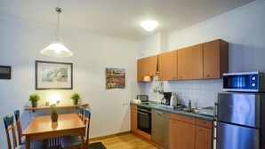 Une cuisine compacte avec des meubles en bois, un réfrigérateur en acier inoxydable, un four à micro-ondes et un lave-vaisselle. On y trouve une table à manger avec des chaises et un luminaire suspendu.