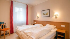 Ein Hotelzimmer mit zwei Betten, einem Schreibtisch, einem Stuhl und einem Fenster mit Vorhängen.