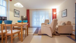 Ein Wohnzimmer mit einer Couch, zwei Sesseln, einem Esstisch mit Stühlen, einem Fernseher und einem Kamin.