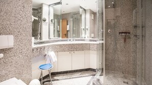 Un baño moderno con ducha de vidrio, lavamanos con espejo y un taburete pequeño.