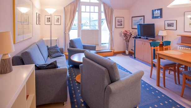 Una sala moderna con sofá, sillones, una mesa de centro, televisor y un comedor con mesa y sillas.