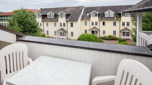 Un balcón con mesa y sillas, con vistas a una hilera de casas urbanas con tejados a dos aguas y ventanales.
