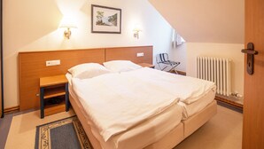 Un dormitorio con cama, mesita de noche, lámpara, silla, radiador y un cuadro en la pared.