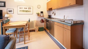 Una cocina compacta con armarios de madera, una mesa de comedor con sillas, una cafetera y un reloj en la pared.