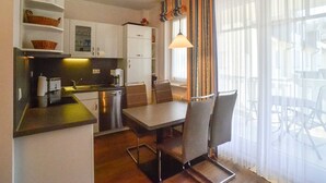 Een kleine keuken met een eethoek, voorzien van een moderne kookplaat, een koffiezetapparaat en een eettafel met stoelen.