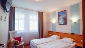 Een hotelkamer met twee bedden, een stoel, een televisie en een schilderij aan de muur.